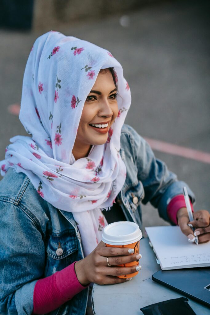 Woman sitting at a table smiling with 
a cup of coffee and writing in a notebook with a human touch.