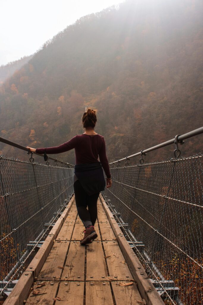 Woman walking across a narrow bridge stepping outside her comfortable zone