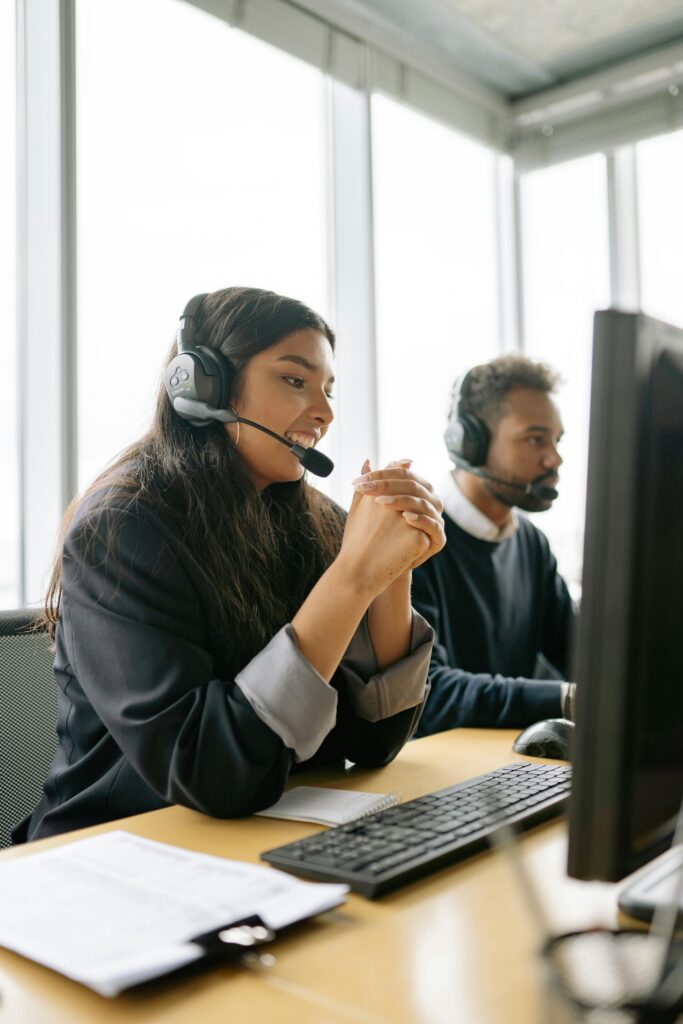 Woman wearing a headset in front of a computer smiling into her computer monitor as an example of the AI vs human connection.