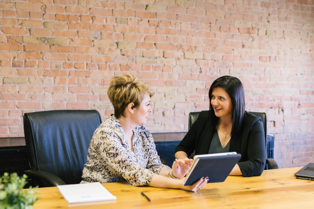 Woman talking with her colleague at a conference table smiling, exhibiting emotional intelligence.