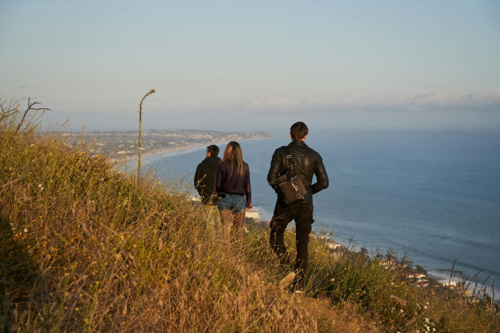 Two men and one woman living abroad walking on a hillside overlooking a town and the ocean