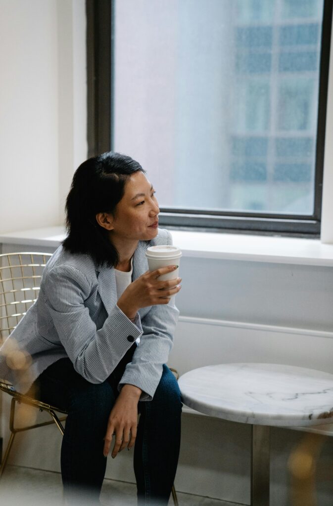 Woman practicing self-care strategies by taking a break, looking out a window drinking coffee