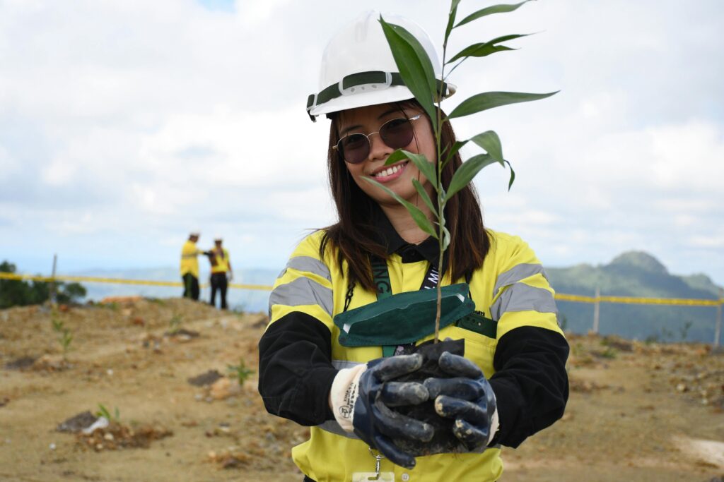 Women getting ready to put a plant a young tree into the ground, one of her Community related goals.